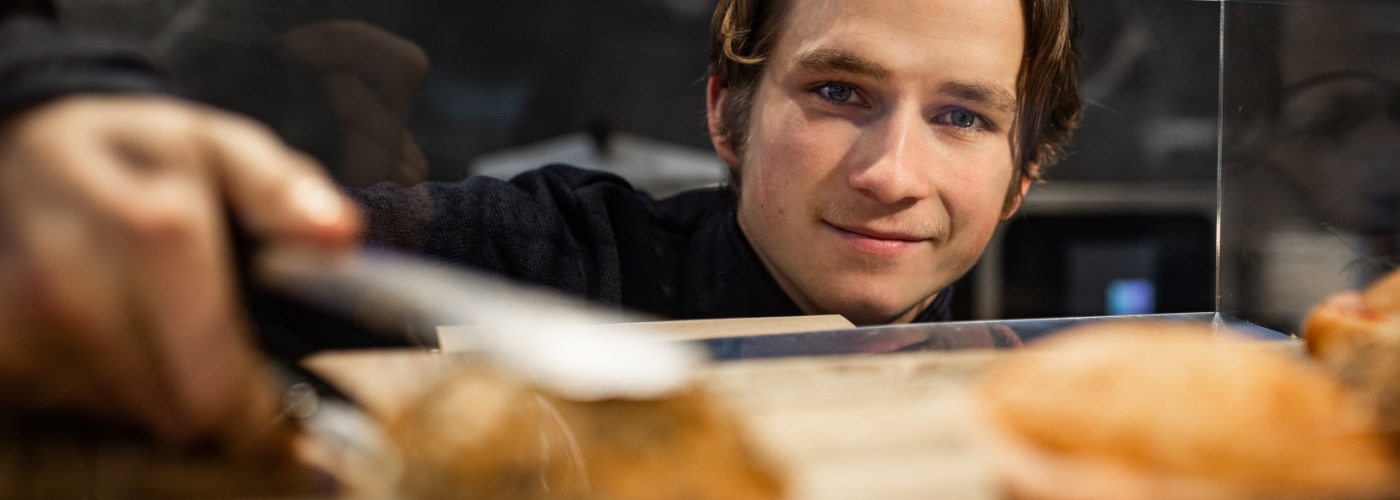 Mikkel kigger smilende mod dig gennem en glasmontre