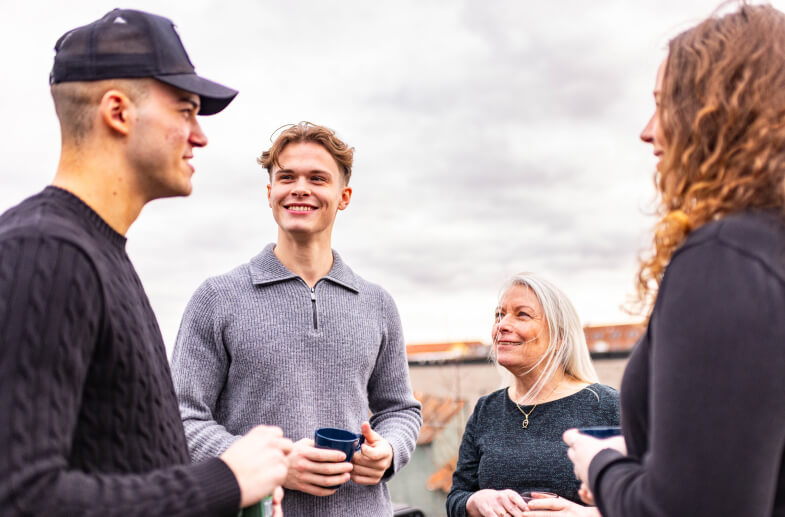 Gruppe billede af fire medarbejdere der står på tagteresse med kaffe