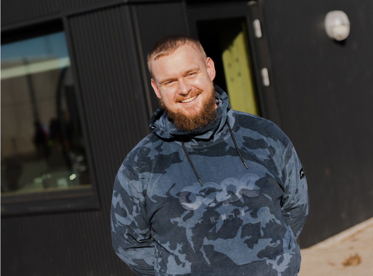 Niklas, mandlig pædagog, står udenfor og smiler til kameraet med hænderne bag ryggen