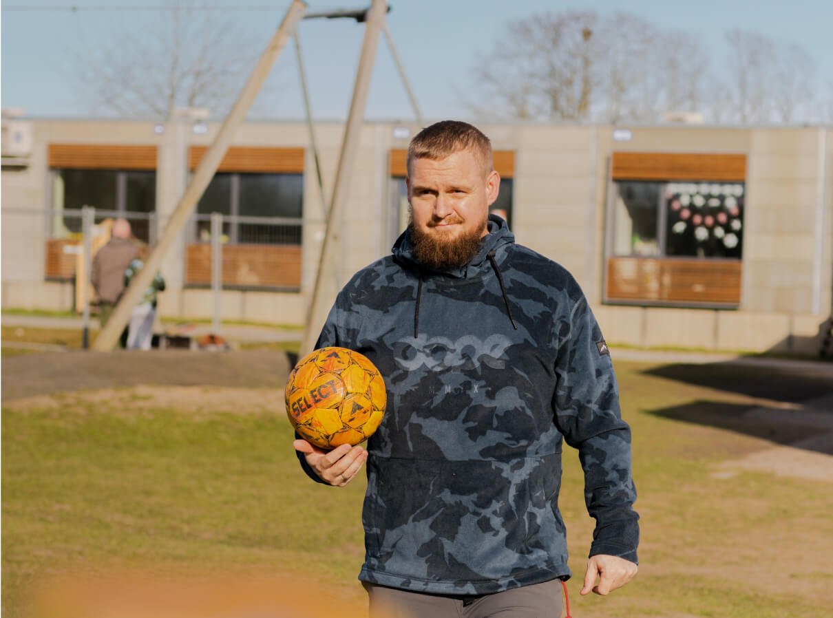 Niklas, mandlig pædagog, går rundt ude på legepladsen med en fodbold i hånden