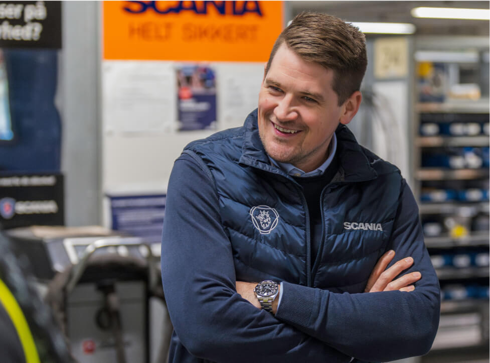 Mandlig medarbejder med Scania vest på, har armene over kors og smiler
