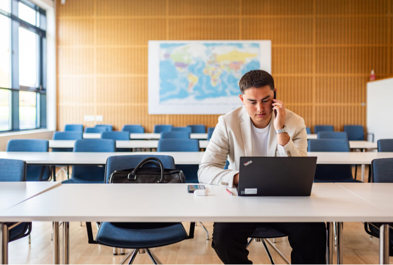 Mandelig elev fra Kuehne + Nagel sidder og taler i telefon, imens han kigger ned på din bærbar skærm.