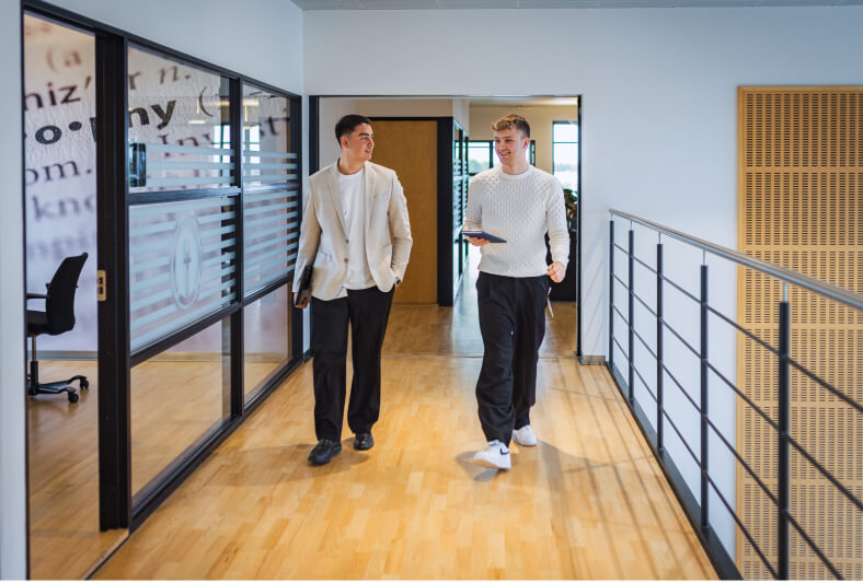 To mandelige elever fra Kuehne + Nagel går ned af gang med hver deres laptop i hånden.