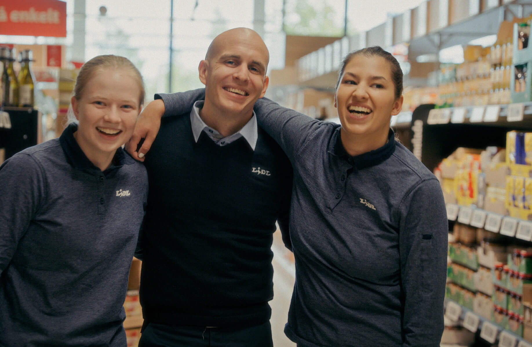 Tre Lidl-medarbejdere står med armene om hinanden i butikken og smiler og griner