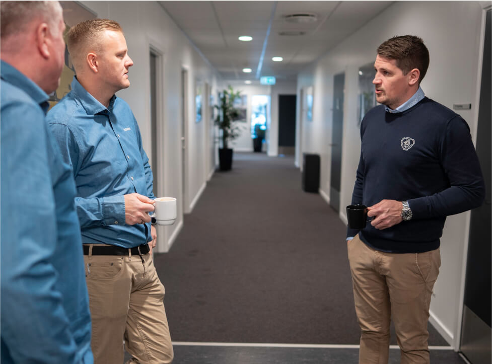 Tre mandlige medarbejdere snakker sammen ude på gangen hos Scania